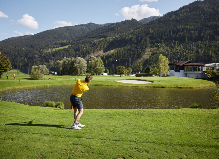 Golfer schlägt Ball am Seeufer vor Bergkulisse im Golfclub Mittersill-Stuhlfelden