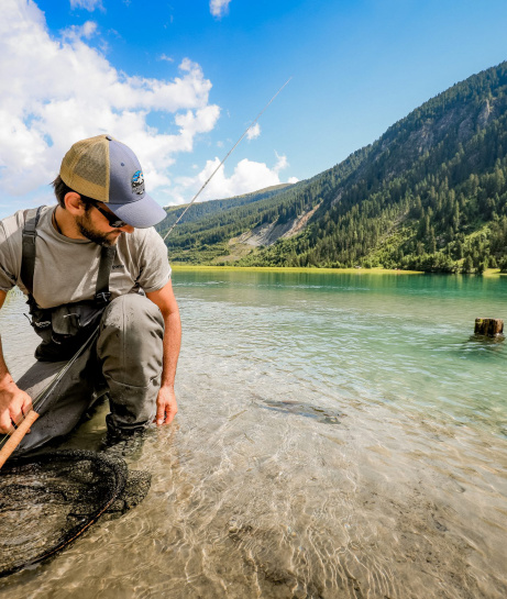 Angler kniet am klaren Bergsee mit Kescher