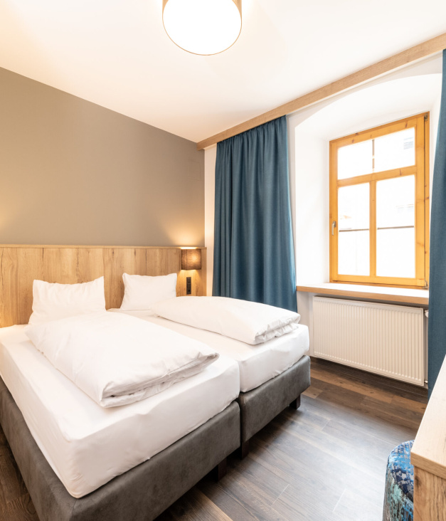 Modernes Hotelzimmer mit zwei Einzelbetten, Holzmöbeln und Fenster mit blauen Vorhängen