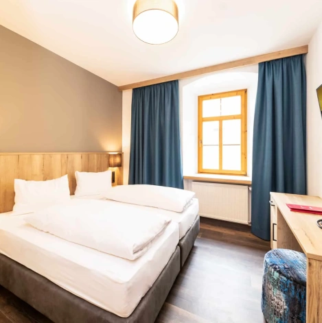 Modernes Hotelzimmer mit Doppelbett, Schreibtisch, TV und Fenster mit blauen Vorhängen