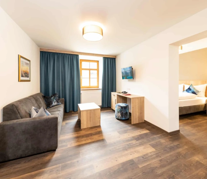 Modernes Hotelzimmer mit Sofa, Schreibtisch, Fernseher und separatem Schlafzimmer