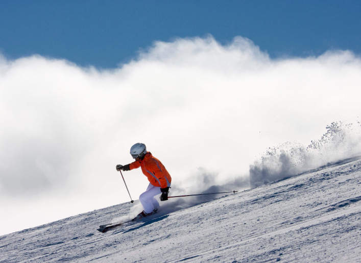 Skifahrer in orangefarbener Jacke auf verschneiter Piste