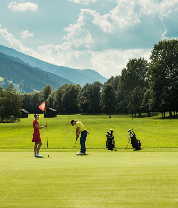 Zwei Personen spielen Golf auf grünem Platz in Berglandschaft