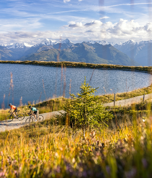 Zwei Radfahrer auf Bergweg am See mit Alpenpanorama
