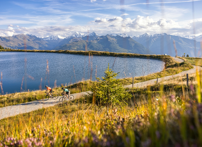 Zwei Radfahrer auf Bergweg am See mit Alpenpanorama