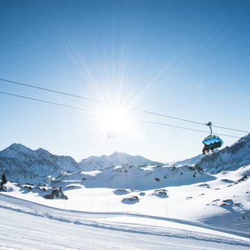 Skilift vor verschneiten Bergen unter strahlender Sonne in Tirol