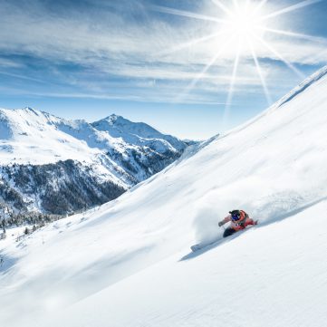 Skifahrer fährt dynamisch eine verschneite Berghangpiste bei Sonnenschein hinab