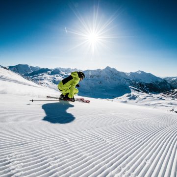Skifahrer in gelber Kleidung fährt bei Sonnenschein auf frisch präparierter Skipiste