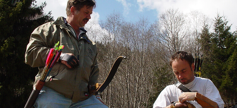 Zwei Bogenschützen im Jagdbogenclub Rauris im Freien, umgeben von Natur.