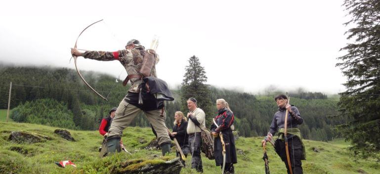 Bogenschütze trainiert im Grünen, umgeben von weiteren Mitgliedern des Jagdbogenclubs Rauris.