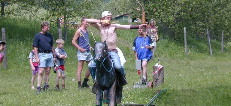 Bogenschütze auf Pferd zielt mit Jagdbogen, umgeben von Zuschauern im Freien.