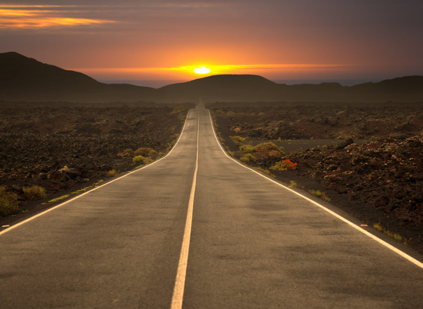 Gerade Landstraße durch Vulkanlandschaft bei Sonnenuntergang, romantische Atmosphäre