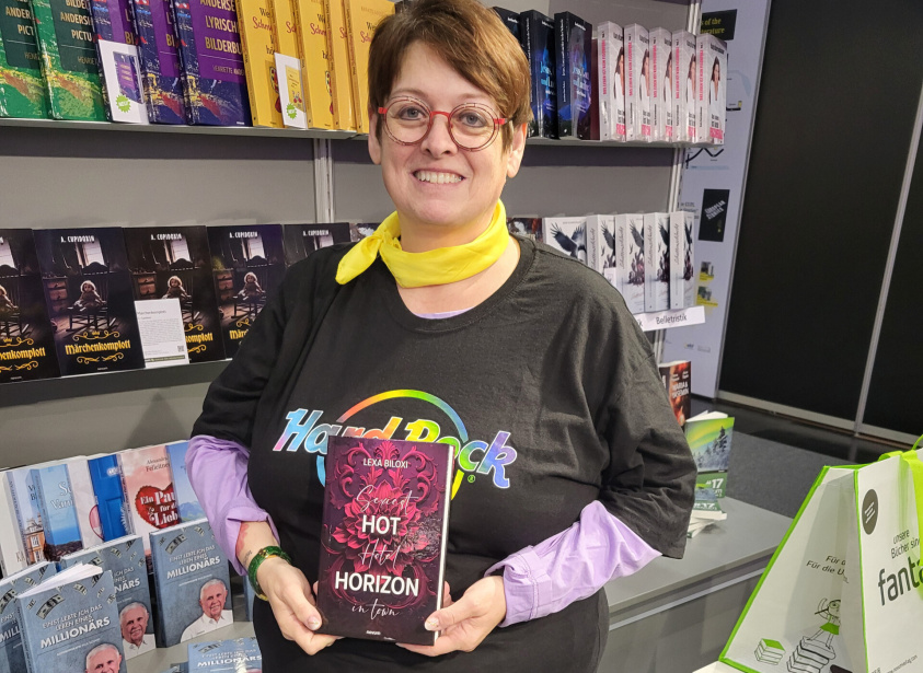 Person hält den Roman Hot Horizon vor einer Bücherwand