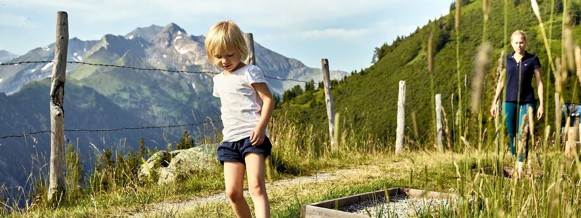 Kind spielt auf dem Weg in den Bergen, Frau genießt die Natur im Hintergrund.