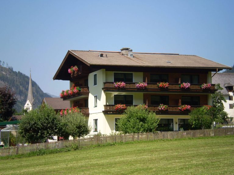 Pension Lindenhof in Rauris mit blühenden Balkonen und Bergblick, umgeben von Grünflächen.