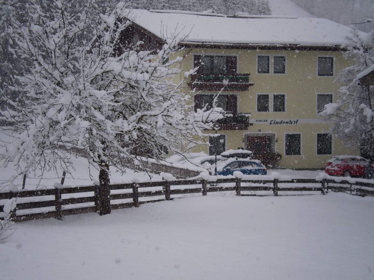 Pension Lindenhof im Schnee mit umliegendem Garten und Parkplätzen, ideal für Skiurlaub.