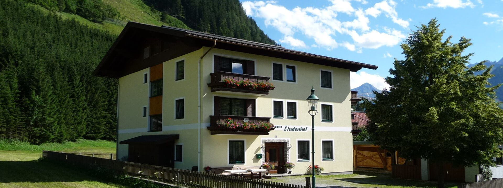 Pension Lindenhof in Rauris mit blühenden Balkonen und Bergblick, umgeben von Grünflächen.