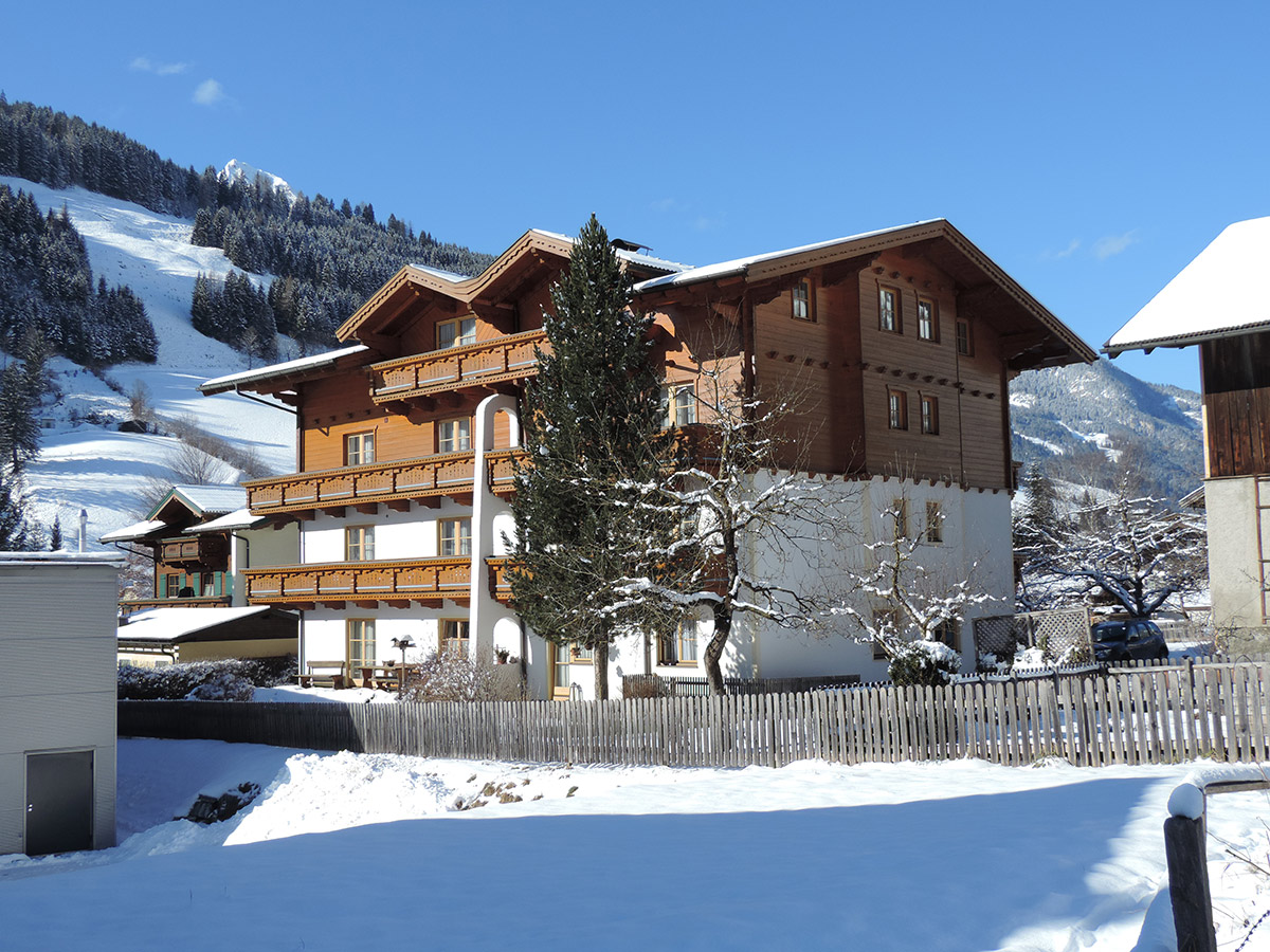Großes Holzhaus mit Balkonen in verschneiter Berglandschaft unter blauem Himmel
