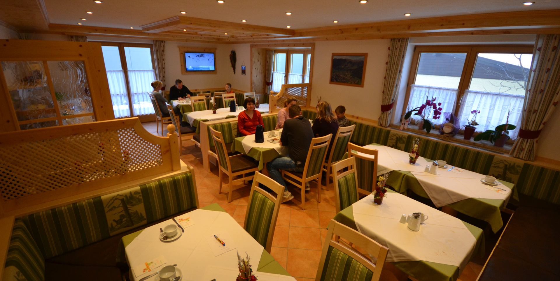 Frühstücksraum mit Holzmöbeln, gedeckten Tischen und Gästen an mehreren Sitzgruppen