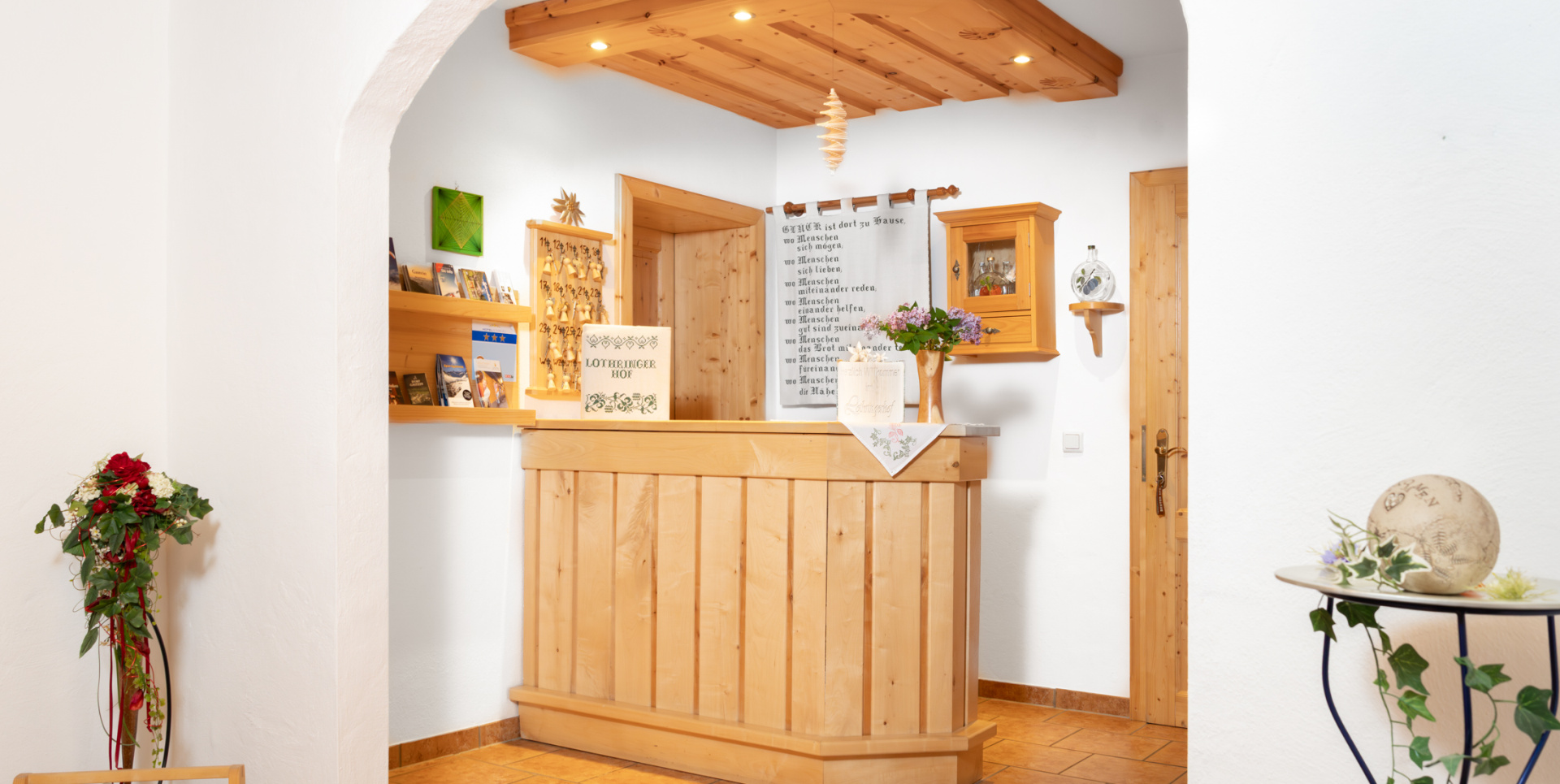Helle Hotelrezeption mit Holztheke, weißem Rundbogen, Prospekten und Blumendekoration
