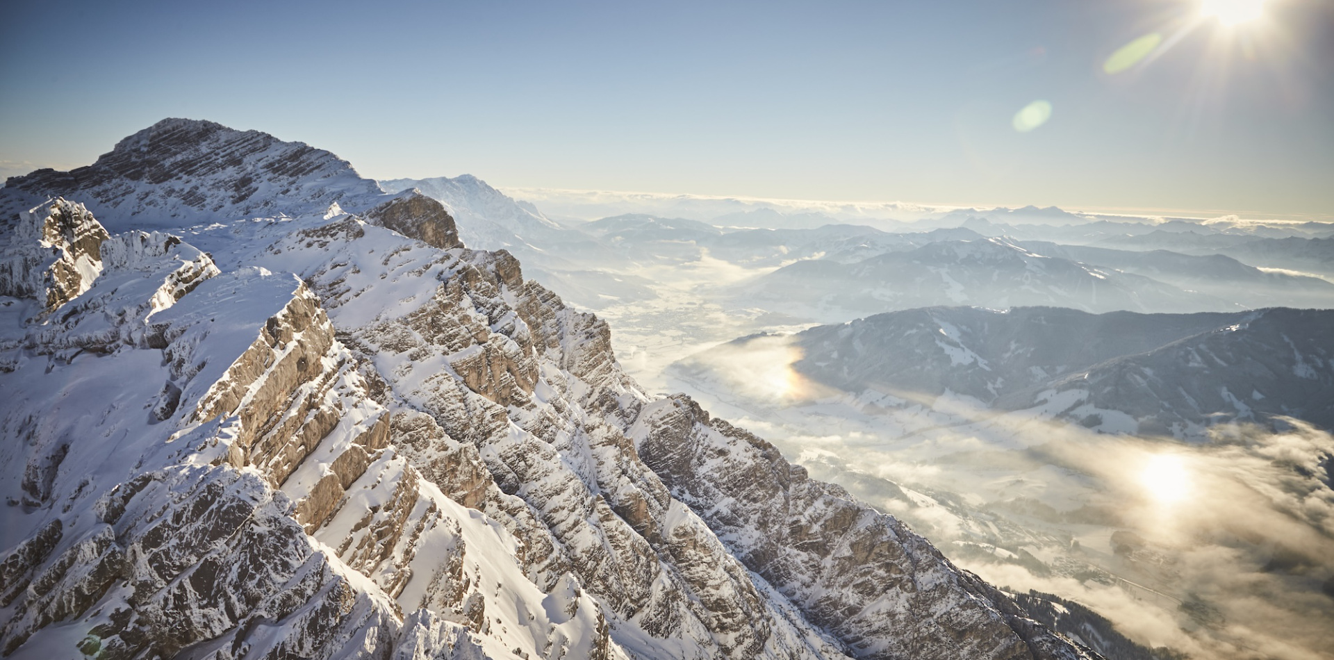 Verschneite Berggipfel mit weitem Blick über neblige Täler und tief stehender Sonne