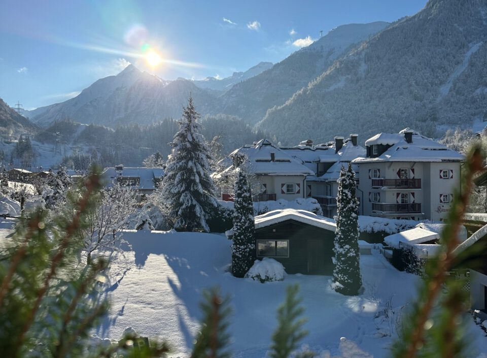 Winterlandschaft mit Sonne über verschneiten Bergen und Häusern