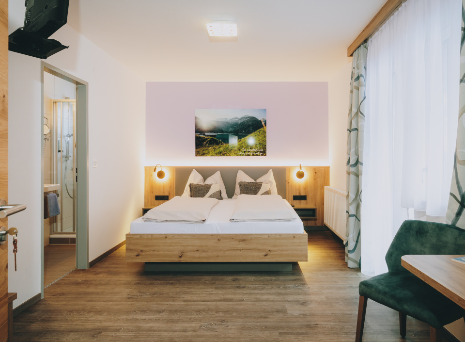 Modernes Doppelzimmer mit Holzbettrahmen, offenem Badzugang, TV und Sitzplatz am Fenster