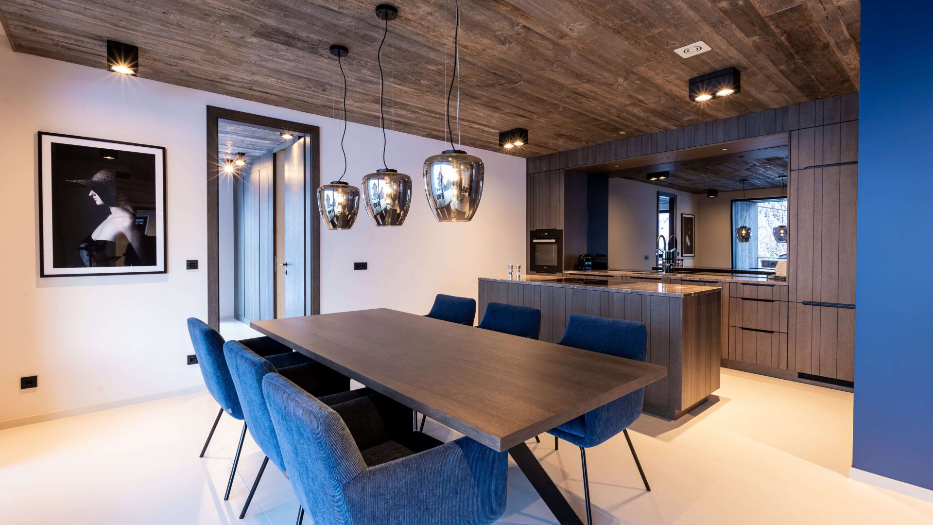 Moderner Essbereich mit blauen Stühlen und offenen Küche im Mountain Chalet Kappl.