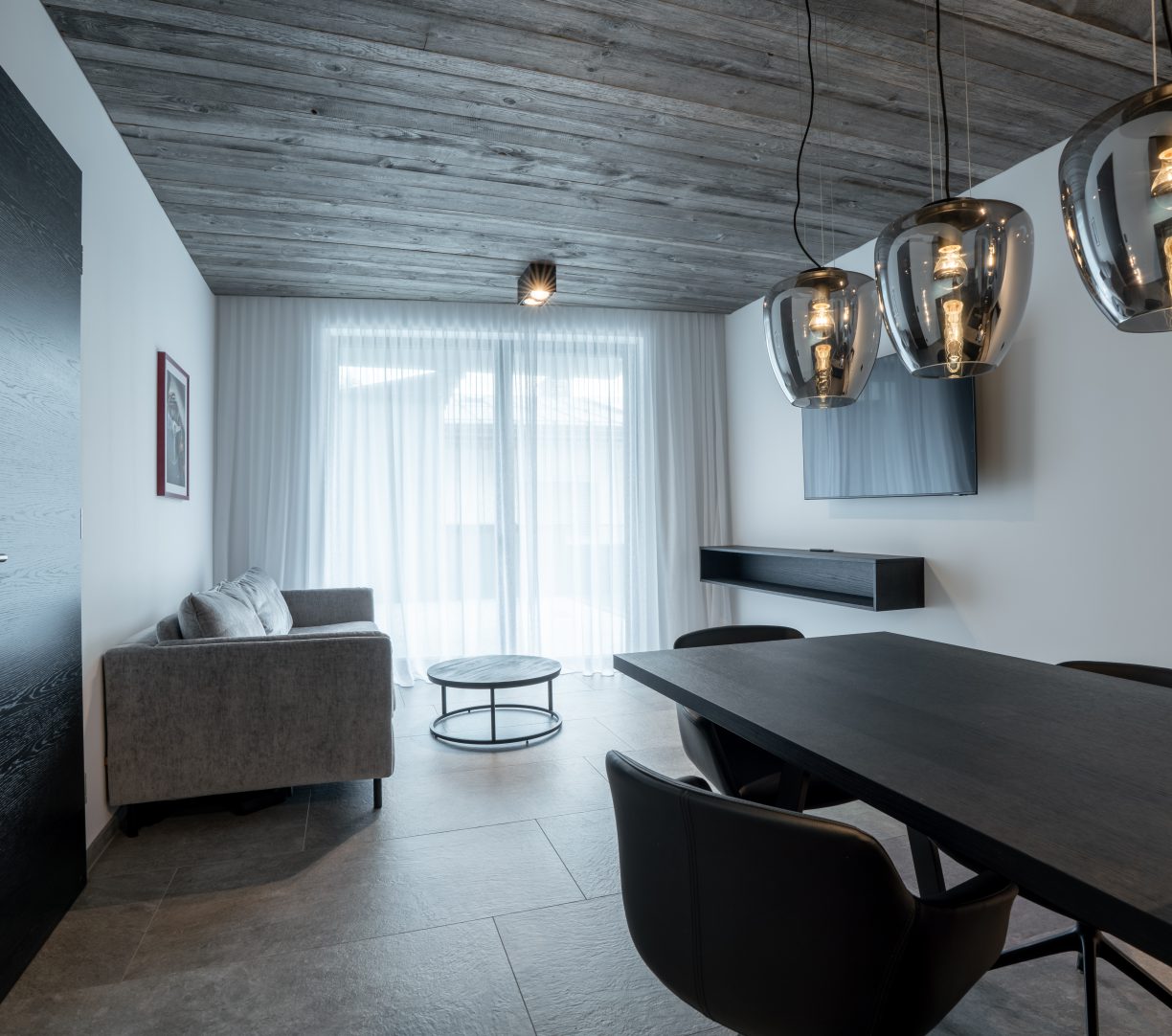 Modernes Wohnzimmer mit grauem Sofa, Esstisch, Designlampen und Holzdecke