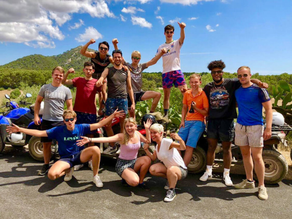 Junge Gruppe posiert fröhlich vor Quads bei sonniger Quad Tour Mallorca für Gruppenevent