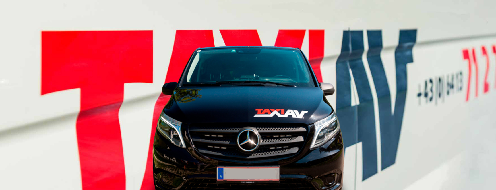 Schwarzes Taxi AV Fahrzeug frontal vor großem Taxi-AV-Schriftzug