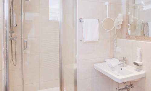 Modernes Hotelbad mit ebenerdiger Dusche, Waschbecken, Spiegel und Handtuchhalter