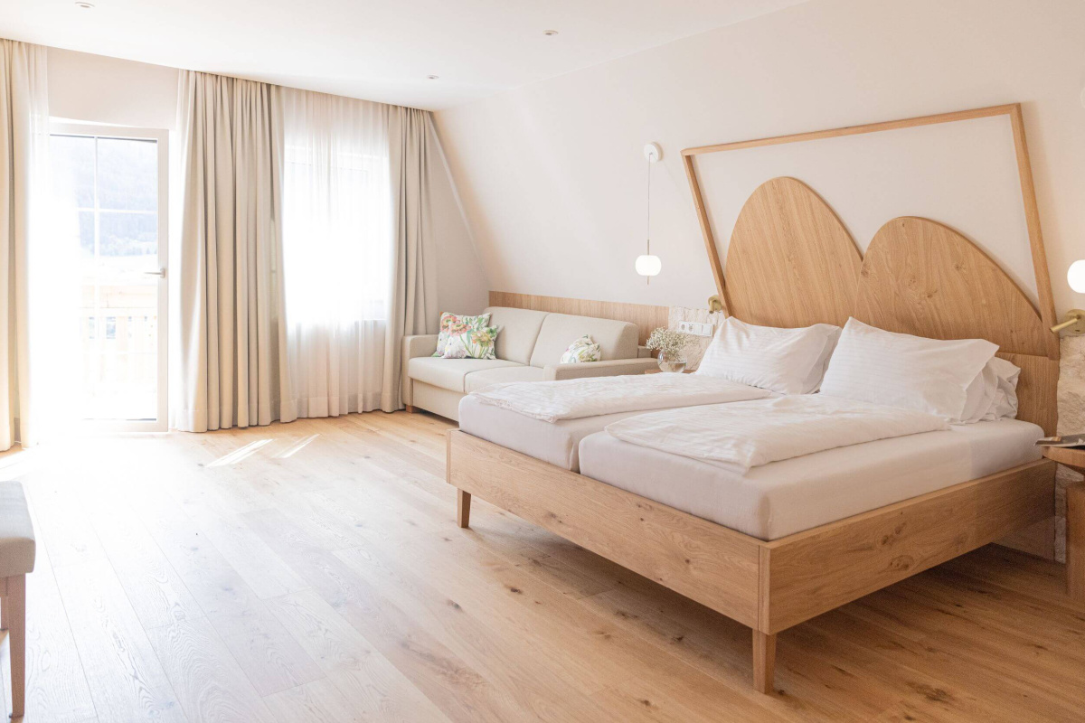Helles Hotelzimmer mit Doppelbett Holzboden Sofa und Balkon im Lungau