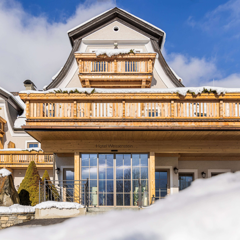 Hotel im Lungau mit Holzfassade und Balkon im Winter vor blauem Himmel