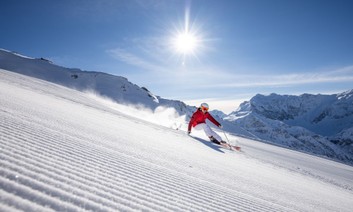 Skifahrer auf sonniger Piste in verschneiter Berglandschaft