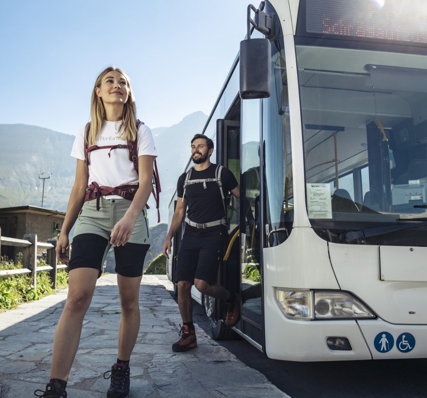 Wanderer steigen an einer Bergstraße aus einem Linienbus